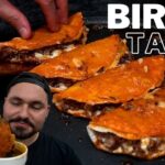 Imagen de tacos de birria: varios tacos dorados rellenos de carne sobre una plancha, con una persona sumergiendo uno en un tazón de consomé y el texto "BIRRIA TACOS". - Recetas Chidas