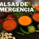 Imagen de cinco salsas servidas en pequeños recipientes de piedra sobre una mesa negra, rodeadas de ingredientes como chiles verdes, tomates, ajos y un aguacate, con texto grande '5 salsas de emergencia' en verde y blanco. - Recetas Chidas