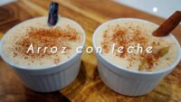Dos ramequines con arroz con leche cremoso espolvoreado con canela; uno de ellos tiene una rama de canela. Sobre la imagen aparece el texto "Arroz con leche". - Recetas Chidas