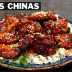Alitas chinas glaseadas de pollo servidas sobre arroz blanco en un plato azul, decoradas con semillas de sésamo y cebollín. El texto "ALITAS CHINAS" aparece en la parte superior izquierda de la imagen. - Recetas Chidas