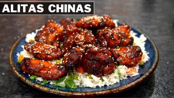 Alitas chinas glaseadas de pollo servidas sobre arroz blanco en un plato azul, decoradas con semillas de sésamo y cebollín. El texto "ALITAS CHINAS" aparece en la parte superior izquierda de la imagen.