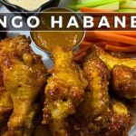 Plato de alitas de pollo cubiertas con salsa mango habanero acompañadas de bastones de zanahoria y apio y salsa dip en el centro, con texto sobrepuesto 'MANGO HABANERO'. - Recetas Chidas