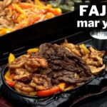 Plato caliente de fajitas mar y tierra con carne, camarones y pimientos de colores servidos en una sartén de hierro sobre una tabla, con texto 'FAJITAS mar y tierra' en blanco. - Recetas Chidas