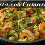 Sartén con pasta fusilli salteada con camarones, trozos de tocino y perejil. En la parte superior de la imagen aparece el texto "Pasta con Camarones". - Recetas Chidas