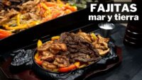 Plato caliente de fajitas mar y tierra con carne, camarones y pimientos de colores servidos en una sartén de hierro sobre una tabla, con texto 'FAJITAS mar y tierra' en blanco. - Recetas Chidas