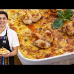 Chef sonriente sosteniendo una rebanada de lasaña de camarón frente a una fuente grande de lasaña adornada con camarones y hojas de albahaca. - Recetas Chidas