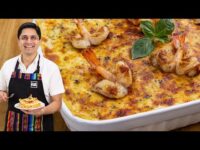 Chef sonriente sosteniendo una rebanada de lasaña de camarón frente a una fuente grande de lasaña adornada con camarones y hojas de albahaca. - Recetas Chidas